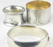 Семь различных серебряных кольца для салфеток с клеймами, включая простой дизайн, цветочный узор, геометрический узор, монограммный дизайн, бисерный дизайн, филигранный дизайн и молотковый дизайн.
